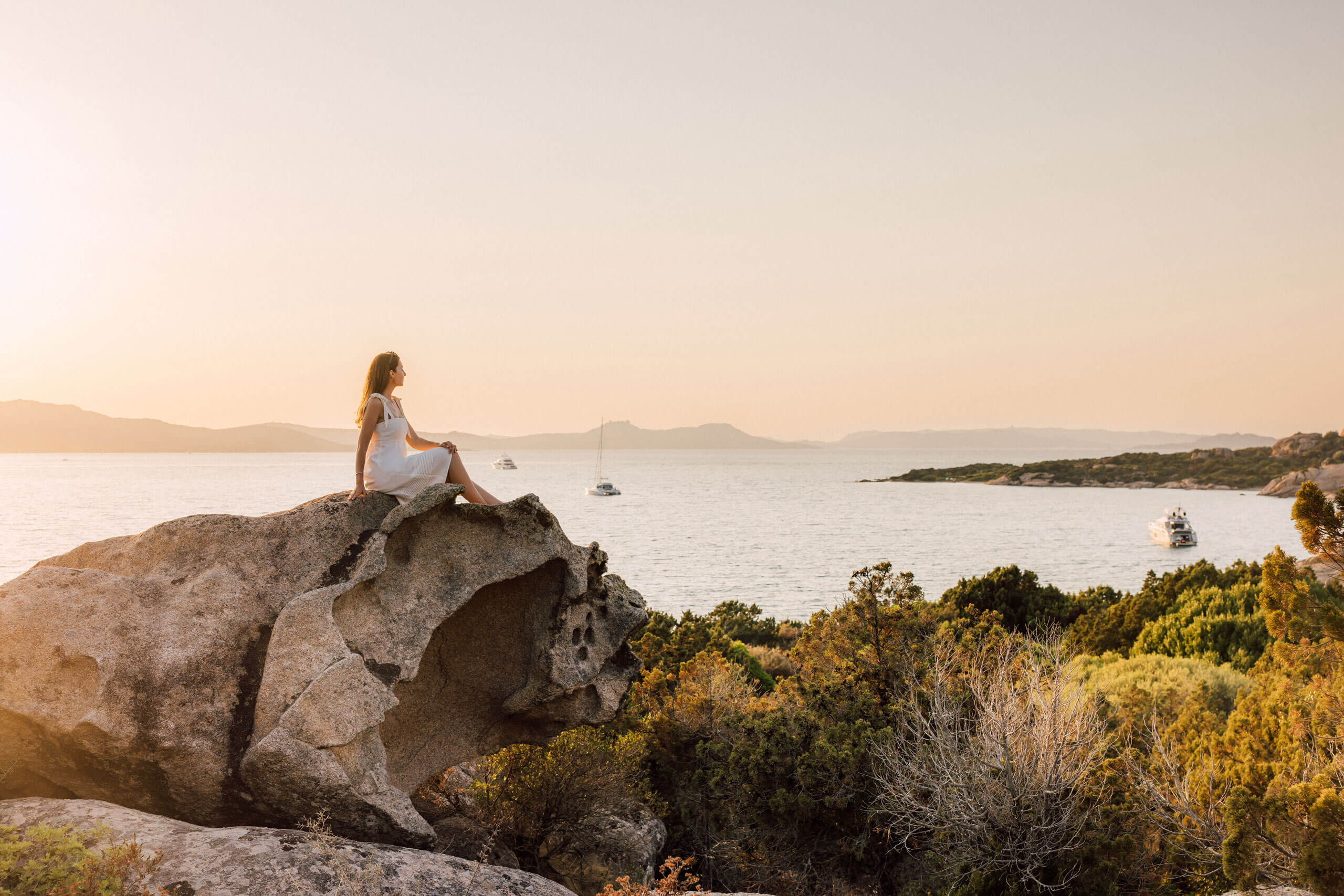 Frau sitzt auf einem Felsen mit Blick auf einen See im Freien, Symbol für überwältigende Gastfreundschaft