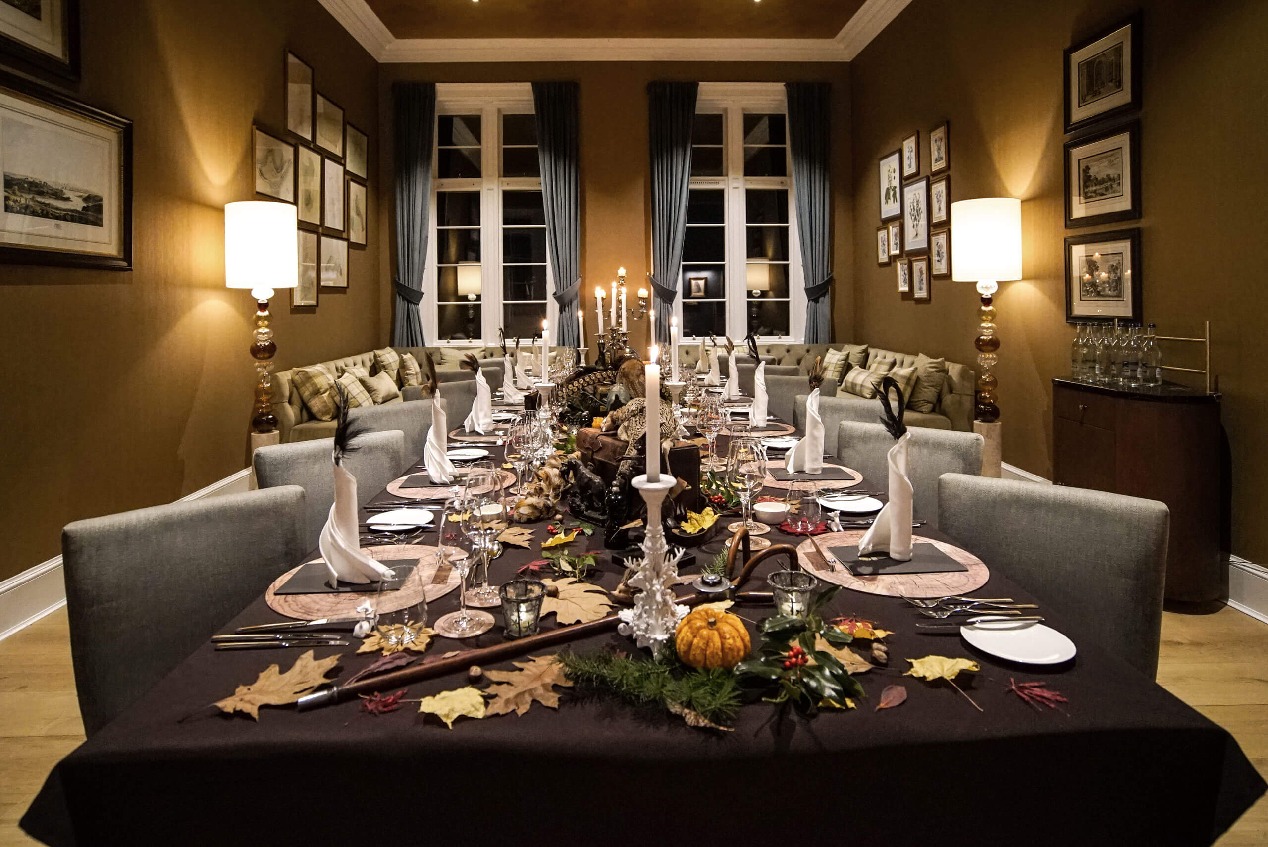 A beautifully set table for a dinner party in an indoor setting with a vase as the centrepiece, complemented by a chair and a couch in the background. Image courtesy of 12. 18. Investment Management GmbH via 12-18.com