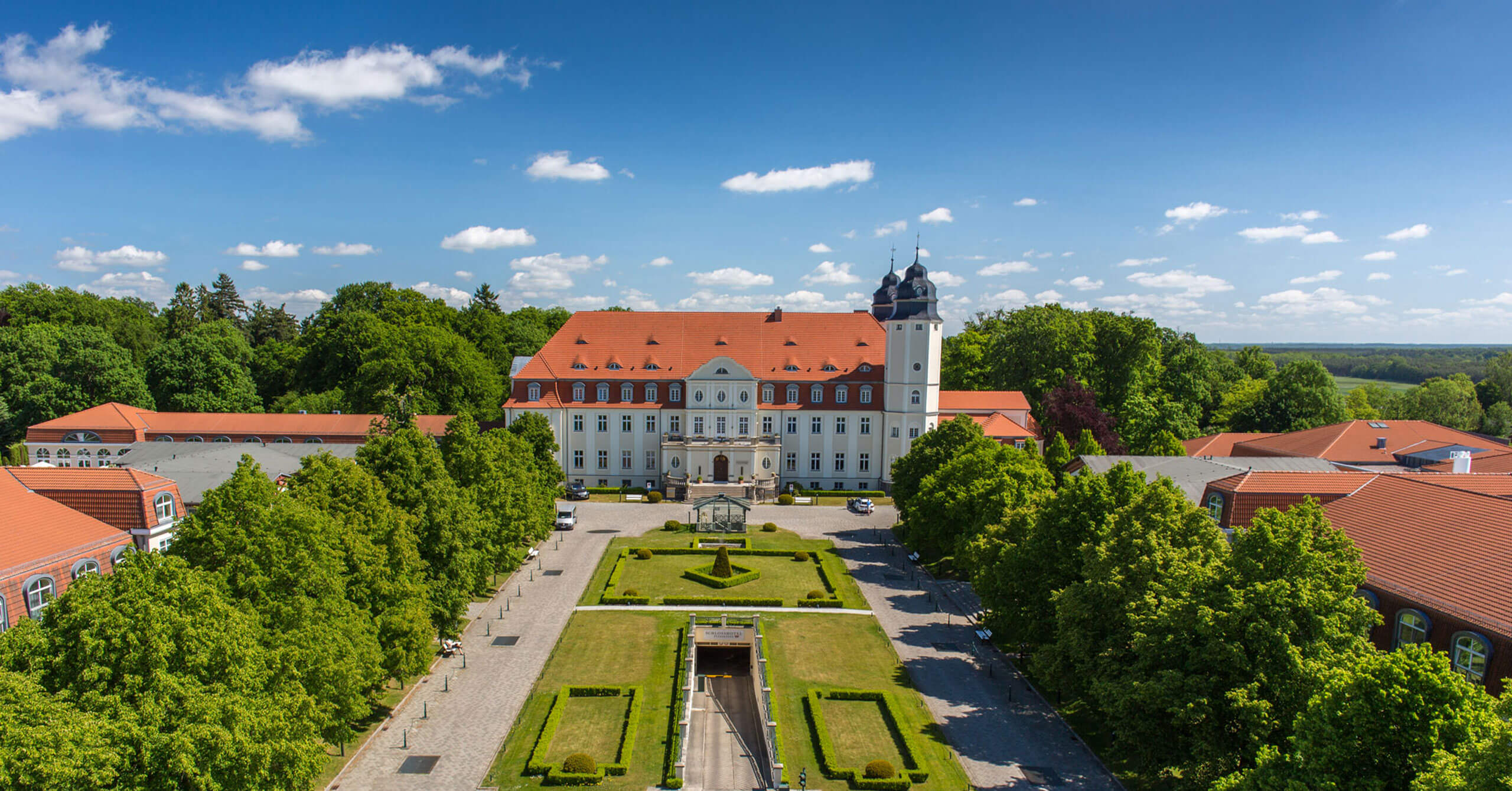 Großes Gebäude mit rotem Dach und weißem Turm umgeben von Bäumen unter bewölktem Himmel