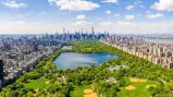 Ein See umgeben von der Stadt San Carlos, New York, mit Wolkenkratzern und grünen Bäumen unter einem bewölkten Himmel, aufgenommen aus der Vogelperspektive.